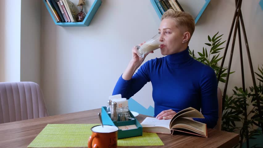 A woman reading a paper book over a cup of coffee in a cafe.