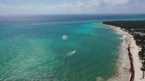 Aerial landscape view of an parasailing parachute inflight - pulled by a speedboat sailing in turquoise water near a tropical coastline - aerial video footage