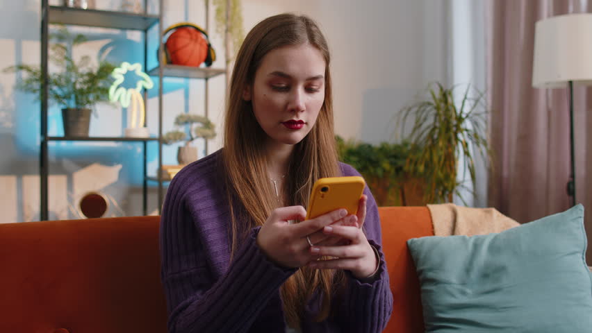 Sad displeased woman use smartphone typing browsing, loses becoming surprised sudden lottery results, bad news, fortune loss, fail, deadline, virus. Portrait of young girl at home living room on couch Royalty-Free Stock Footage #1102630131