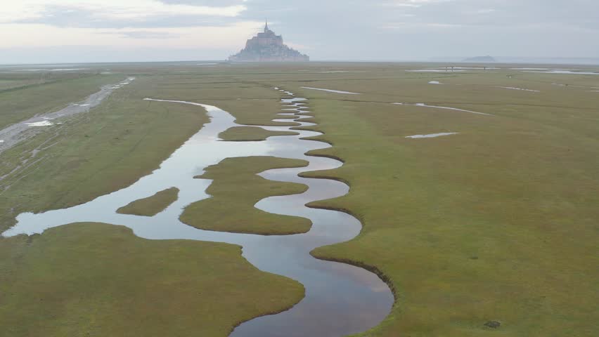 
Beautiful view of famous historic Le Mont Saint-Michel tidal island with  fresh green grass and ponds on a sunny day with blue sky and clouds in summer, Normandy, northern France
