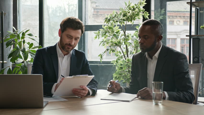 Two diverse multiracial businessmen signing document agreement shaking hands success business deal. Multiethnic men partners in office meeting handshake satisfied agree sign loan investment contract Royalty-Free Stock Footage #1102636031