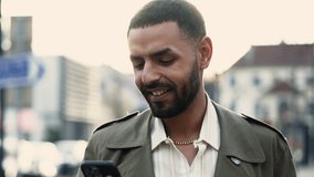 portrait of an Arab man standing in a city street while checking his phone. The clip is a close-up of the subject's face and the urban environment is visible in the background