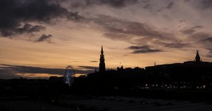 Timelapse video at sunset of Edinburgh skyline from the top of the Waverley Station, the Scott Monument and the Ferris Wheel can be clearly seen over the orange sky with clouds moving fast.