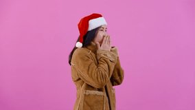 4K, portrait, Long-haired Asian girl in brown sweater wearing Christmas hat, bring both palms together, crossed arms, alternately, to alleviate the cold, Isolated indoor studio on pink background.