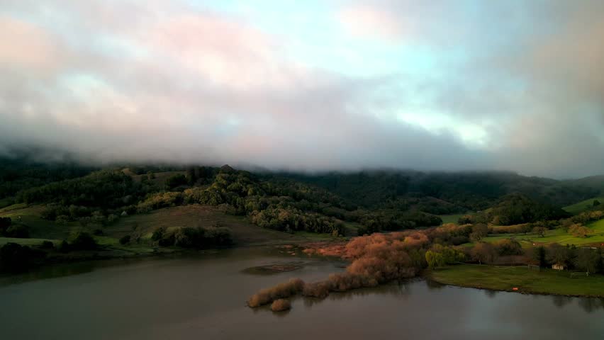 Sunrise color in fog over green hills and lake in hilly California landscape