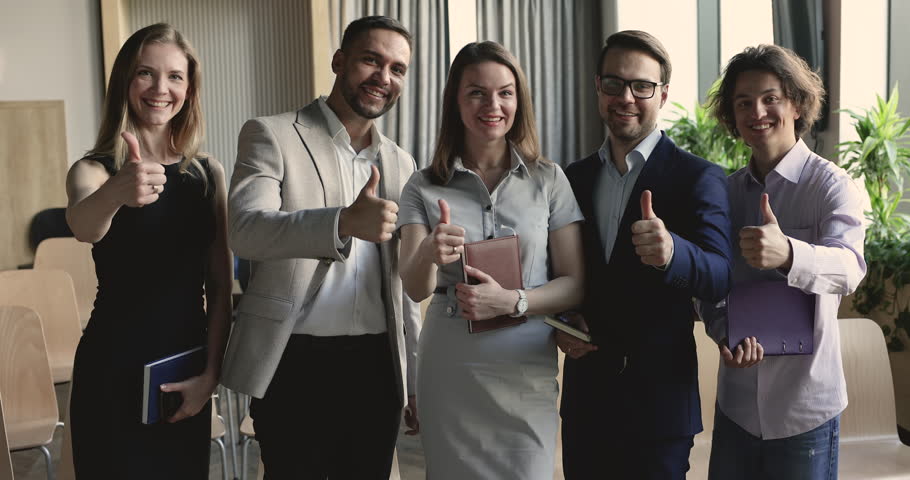 Business team of serious employees standing together, holding notebooks, posing in office, getting cheerful, happy, smiling at camera, making thumb up gesture, showing like