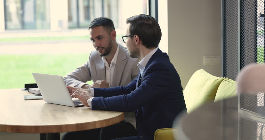 Two confident motivated business partners men using laptop at co-working workplace table, talking discussing Internet project, online presentation. Manager, software developer meeting with client Royalty-Free Stock Footage #1102639697