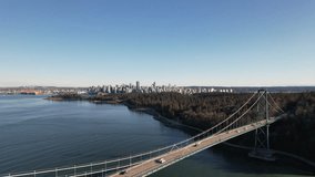Aerial footage of Lions Gate bridge with view of Downtown Vancouver and Stanley Park on a sunny spring day, this footage is flying away from the bridge with the view of downtown in the background