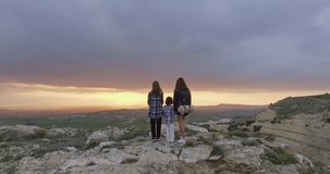 Aerial view of a mother and daughters standing on top of a mountain at sunset. The family admires the nature of the mountains after active hiking. High quality 4k footage