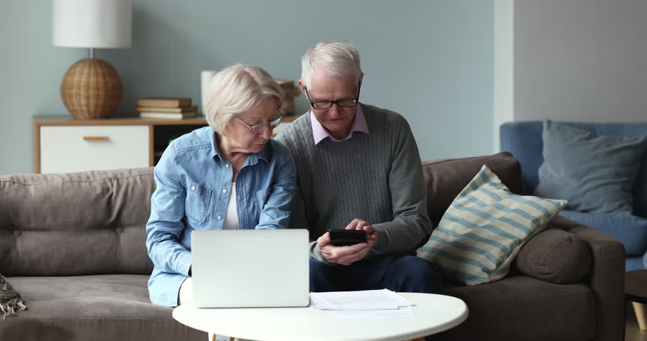 Confused serious older retired couple in glasses calculating monthly expenses, rent, mortgage, insurance, taxes, fees, doing accounting work, using banking, payment app on laptop Royalty-Free Stock Footage #1102645733