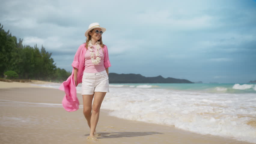 Beautiful elegant American woman wearing traditional Hawaiian lei on sunny Oahu summer beach, Hawaii island USA. Slow motion shot on RED camera 4K. Smiling woman having fun laughing on Hawaii holiday