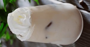 Sprinkling cinnamon powder on Iced coffee latte cocktail in glass, summer cocktail with coffee ice cubes, milk froth and whipped cream on top, slow motion close up video clip, 4k footage