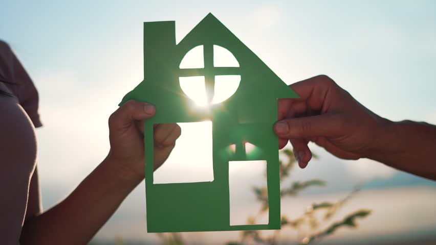 Happy family. People are holding paper house in their hands. Toy house family mortgage symbol. People dream of their own home.Paper house in rays of sun in nature.Happy family walking with paper house Royalty-Free Stock Footage #1102654563