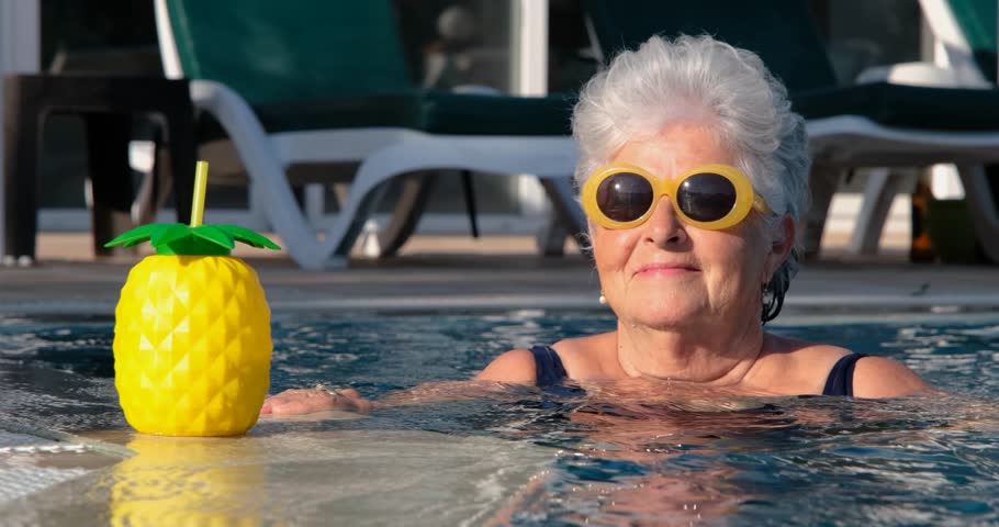 Beautiful elderly lady with fashionable sunglasses in swimming pool, enjoying cocktail. Looking at camera. Tropical summer vacation travel destination. Positive lifestyle background. Set of 13 files. Royalty-Free Stock Footage #1102654773