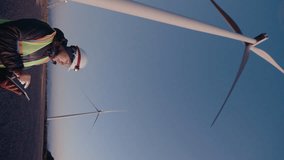 Wind energy engineer in workwear and hardhat working with digital tablet at wind power station early in the morning. Green energy, sustainable living concept. Vertical format clip, side view - Powered by Shutterstock - Get 15% off with code: PIKWIZARD15