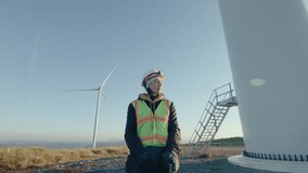 Female renewable energy engineer in workwear and hardhat standing at wind farm in the morning and posing on camera. Zoom shot