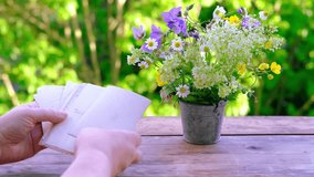 female hands holding paper envelope with old photographs, bouquet of wild flowers on table wooden table in garden, blurred natural background, concept of genealogy, memory of ancestors, family tree - Powered by Shutterstock - Get 15% off with code: PIKWIZARD15