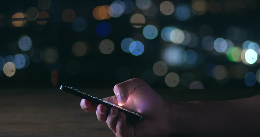Male hand scrolling browsing social networks on phone on background of lights of night city. Cinematic shot male scroll through news feed on mobile app on smart phone. Scrolling social media on phone Royalty-Free Stock Footage #1102663039