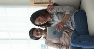 Cheerful pretty mature mother and young adult daughter holding digital gadget, resting on sofa together, using application, payment service on tablet for online shopping