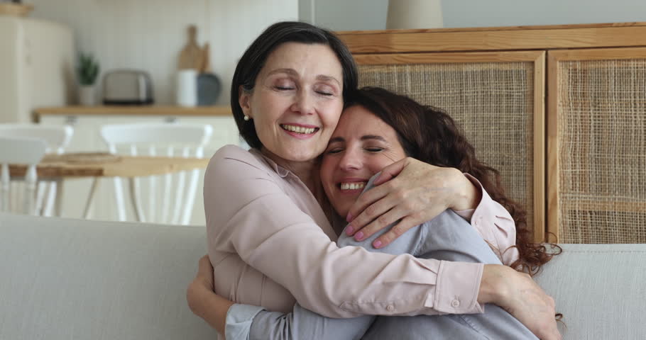Happy middle aged senior mom and adult pretty daughter hugging on sofa at home with love, warmth, tenderness, affection, closing eyes, smiling, enjoying leisure time, family closeness | Shutterstock HD Video #1102664625