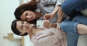 Positive young adult daughter showing online app on smartphone to mature mother, shopping on Internet, watching online content, taking selfie with funny effects, filters