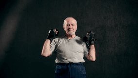 An old elderly man in sportswear is training in the gym doing weight lifting with dumbbells. Leisure healthy lifestyle. An elderly man is exercising. Fitness for the elderly. active pensioners.
