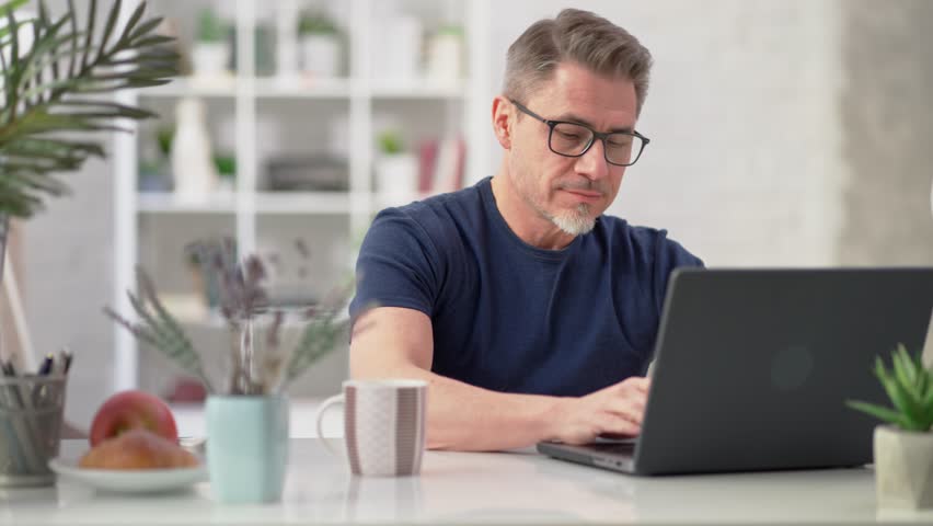 50s businessman with gray hair working from home. Man in casual sitting at desk using laptop computer, business manager online in home office. Royalty-Free Stock Footage #1102672473
