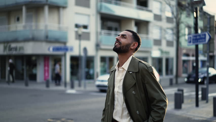 a young Moroccan man of Arab descent standing in a city street and looking up at the sky with a happy and hopeful expression on his face. The shot is a close-up of the subject's face Royalty-Free Stock Footage #1102672931
