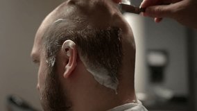 Hair stylist barber is shaving man's hair on the back of head using blade razor.