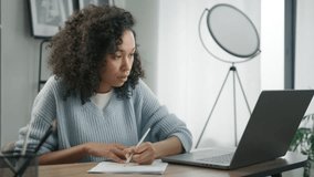 Focused and concentrated african female student e learning online on internet website. Young woman of color working remotely at home office desk, makes notes in work document, looks at laptop computer - Powered by Shutterstock - Get 15% off with code: PIKWIZARD15