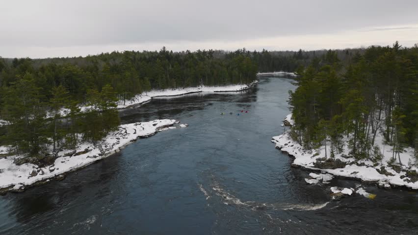 Whitewater kayakers slowly floating down the Ottawa river in winter surrounded by snowy banks and forest