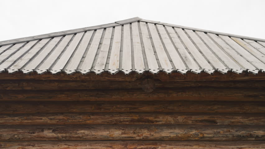Bearded man in knightly clothes walks across courtyard past medieval castle wooden gate. Young warrior walks past white tent patrolling territory carefully