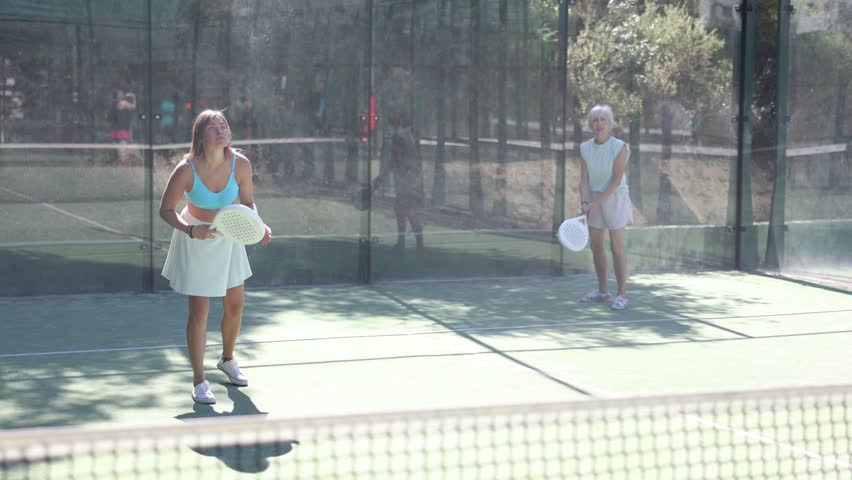 Portrait of emotional fit young woman playing padel tennis on open court in summer, swinging racket to return ball over net. Sportswoman ready to hit volley