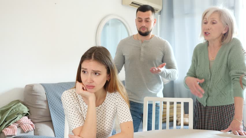 Offended woman sitting on sofa in apartment. Her husband and mother-in-law quarreling with her. Royalty-Free Stock Footage #1102688845