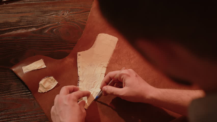 Craftsman shoe tailor applies stencil to leather material.