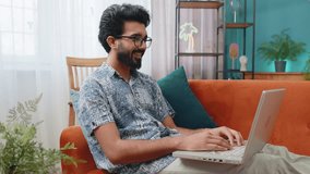 Indian man sitting on couch looking at camera, making video webcam conference call with friends or family, enjoying pleasant conversation. Young hindu guy laughing waving hello at home room