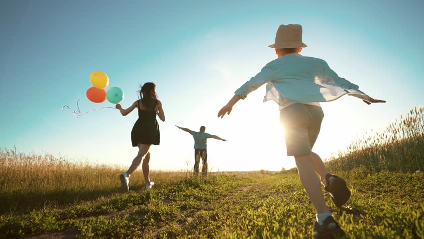 Happy family playing catch-up:child is running in front in center and his parents are running on sides of field holding colored balloons in hands. Outdoor games in summer leisure activity together. Royalty-Free Stock Footage #1102697497