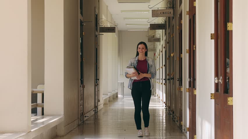 A female college student with a textbook walking along the corridor in the college building. Education, back to school concept. Royalty-Free Stock Footage #1102702793