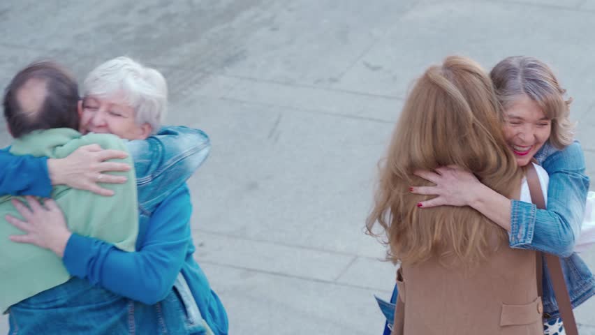 A group of middle-aged friends run into each other on the street and greet warmly. They exchange hugs and catch up on each other's lives. High quality 4k footage 