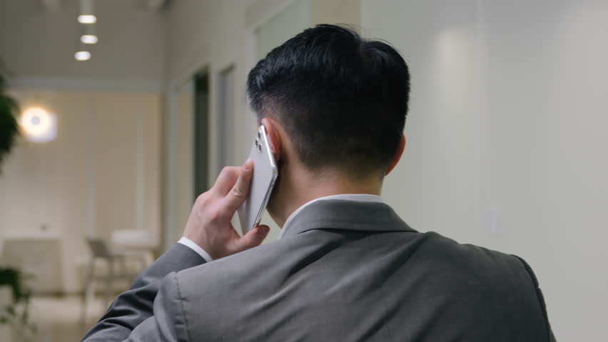 Back view businessman walk in hallway office talk mobile phone. Turn head behind Asian chinese korean man executive manager middle-aged boss talking smartphone negotiate discuss business communication Royalty-Free Stock Footage #1102704775