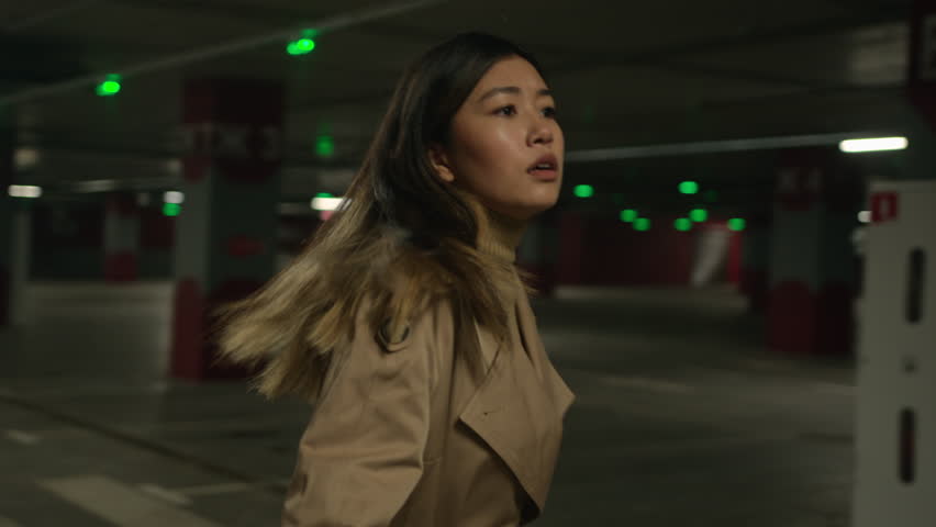 Scared stressful frightened Asian woman walk alone in underground afraid chinese japanese korean girl lost in empty dark parking turn head look around search help run from dangerous fear move hurry