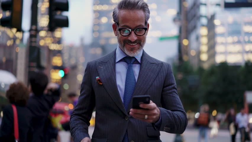 Handsome and Successful business man in stylish suit looking  at smartphone screen while walks outdoors in city. Prosperous smiling entrepreneur in eye glasses feels confident and prosperous  Royalty-Free Stock Footage #1102705847