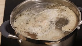 Close up video of hand mixing chicken meat broth water in stainless pan on cooker panel and defoam, remove foam from soup with spoon. Clean cook diet, low calories soup. High angle view, 4k resolution