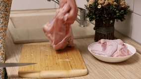 Unrecognizable female in bathrobe cutting, carving chicken meat flesh with knife and putting wings in white plate on wood table in kitchen. Cooking healthy food, meat. Domestic culinary recipe. Video