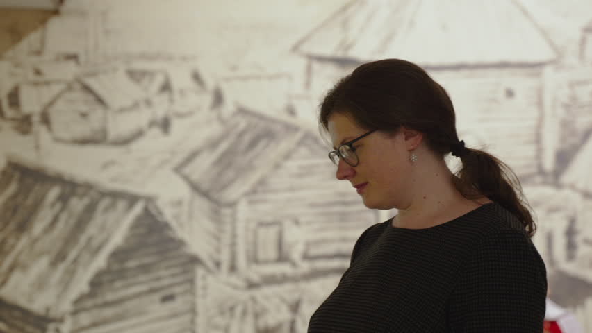 Portrait of young overweight woman with glasses in museum, close-up. Caucasian person alone carefully examines exhibits in museum, slow motion. Visiting exhibition on Museum Day.