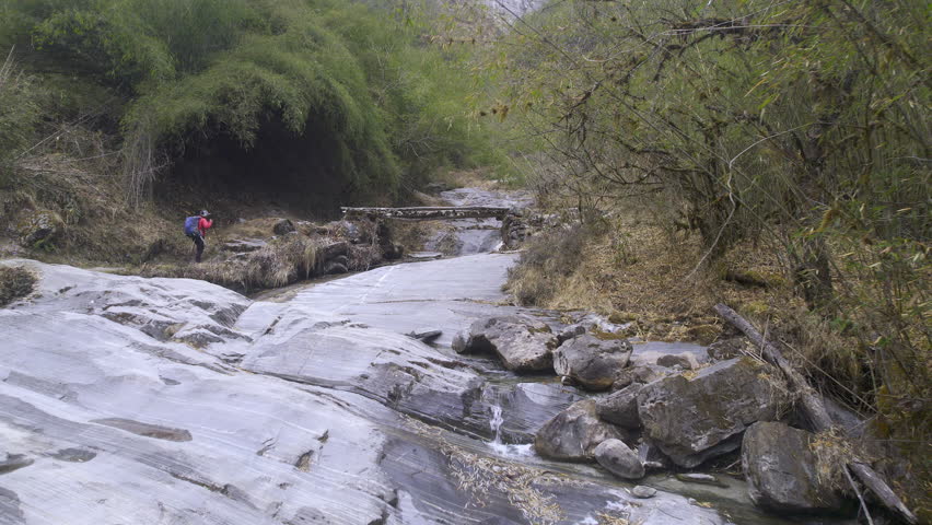 Aerial view flying over creek as man hikes over a bridge on the Annapurna circuit trail in Nepal.