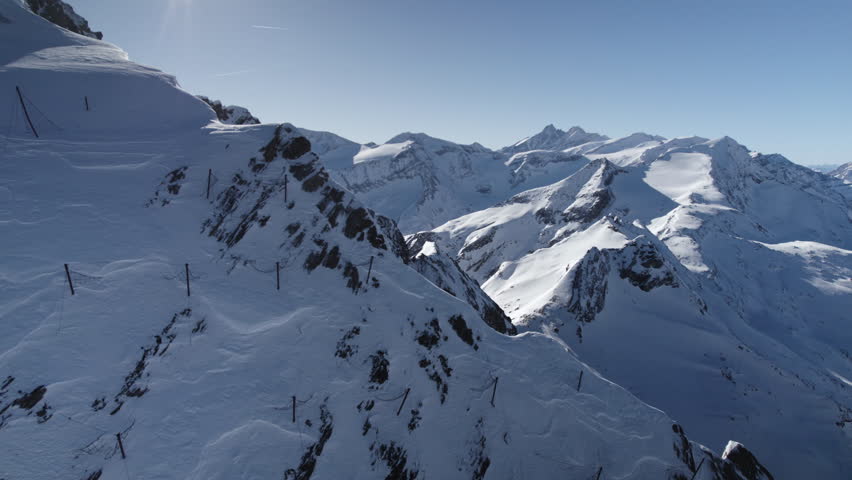 Cinematic forward flight along snowy rocky mountains lighting in sun during winter day in Austria