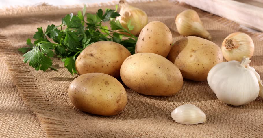 fresh vegetables on burlap. potatoes, onions, garlic, parsley on the table. harvest closeup. farm products on a sunny day. rustic still life