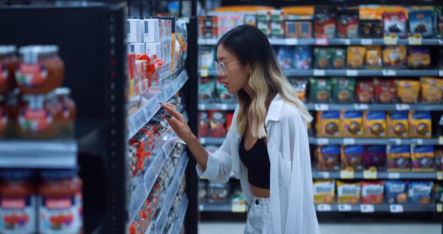 young asian female shopper is frightened at the sight of high food prices while shopping in the grocery supermarket. A woman is unhappy with the increase in food prices in the grocery store
