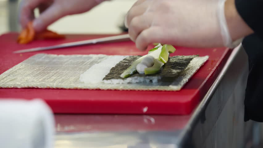 Chef is rolling Japanese sushi at the restaurant kitchen. Chef is using the rolling mat for sushi making at a Japanese restaurant. Chef is putting multiple ingredients in the Japanese sushi roll Royalty-Free Stock Footage #1102735563
